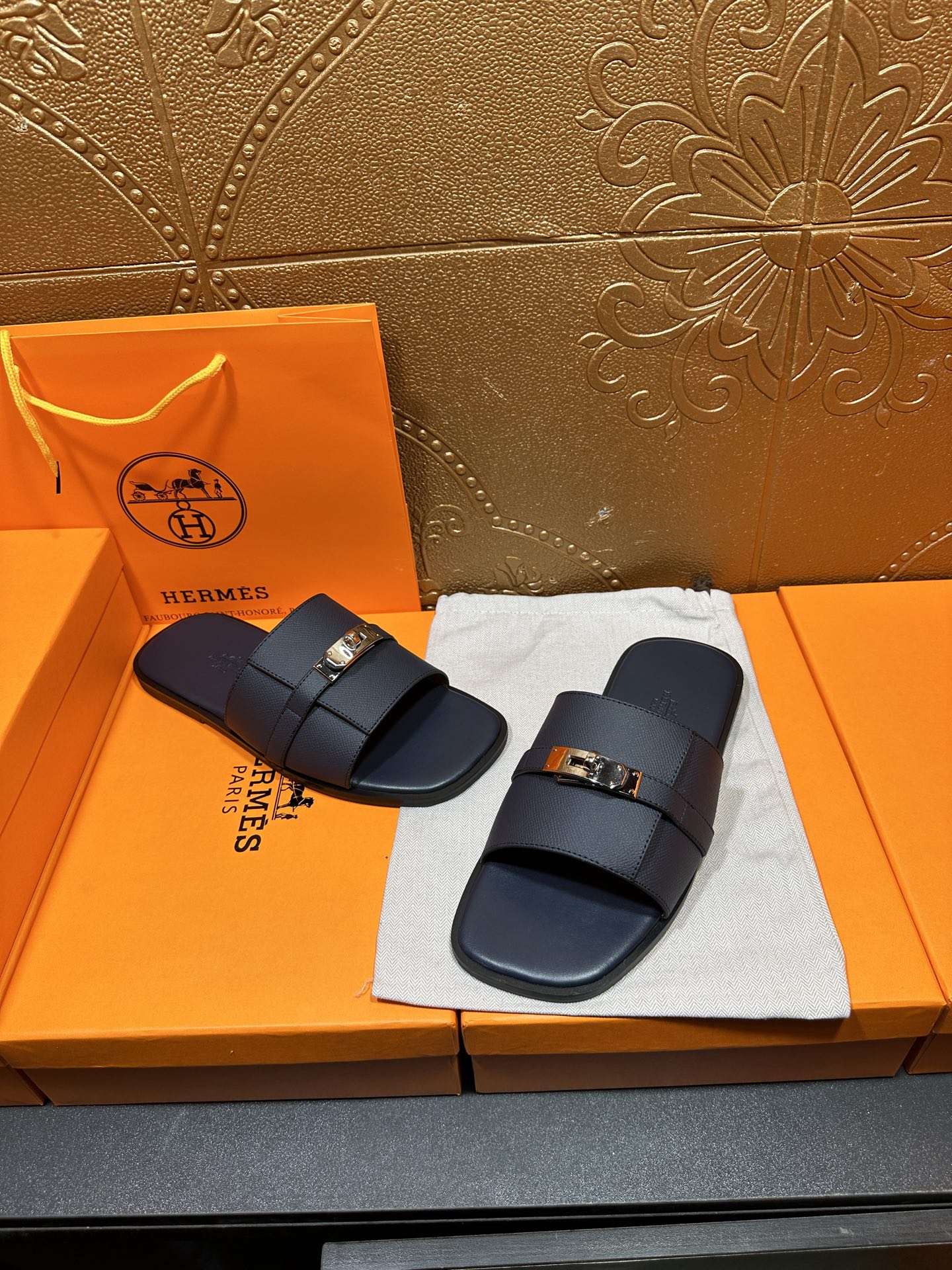 Navy leather slide sandals with gold-tone buckle, placed on white cloth