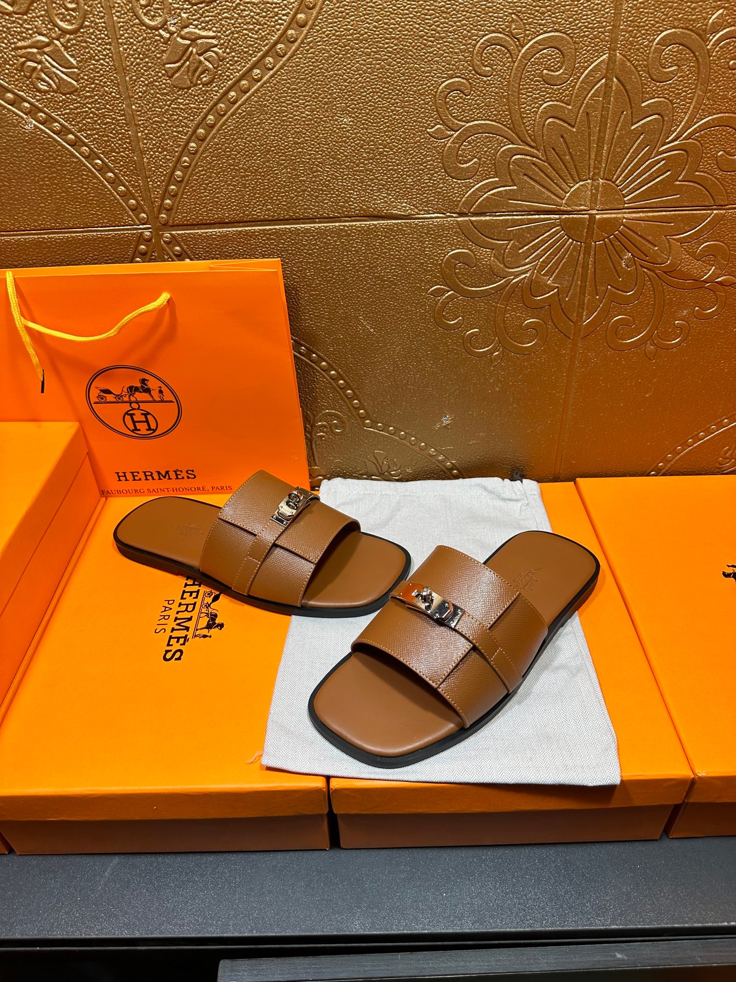 Brown leather slide sandals with two straps and square buckle, on dust bag