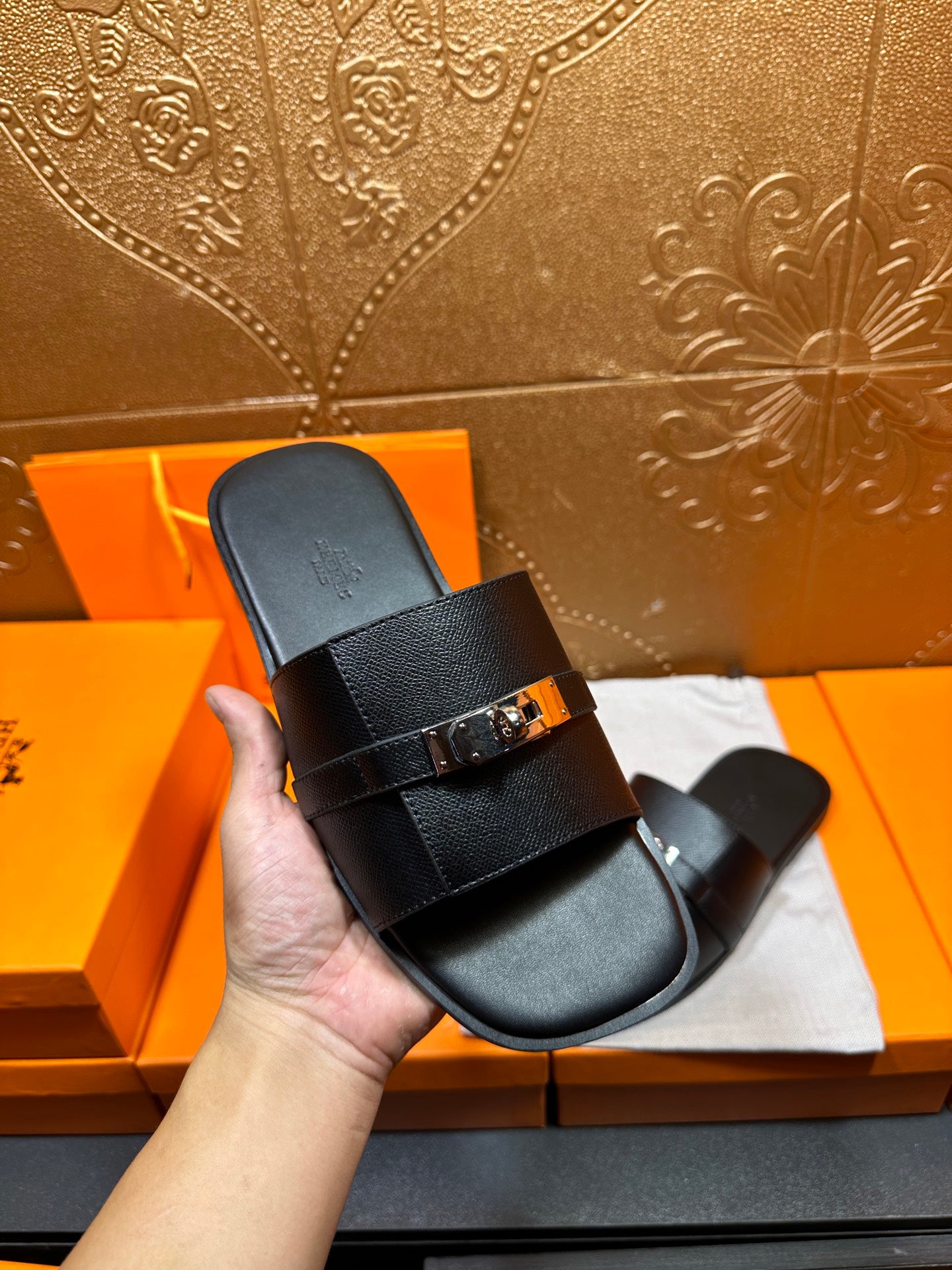 Hermes black leather slide sandal in hand, top strap with gold-tone buckle