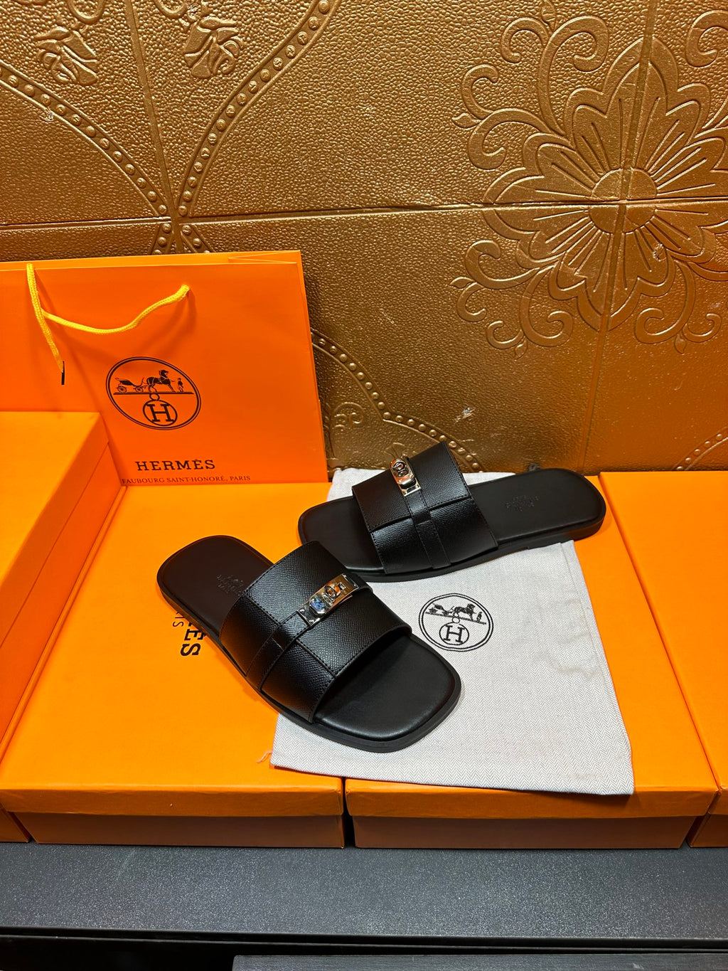 Hermes black leather slide sandals, angled view with gold-tone buckle hardware