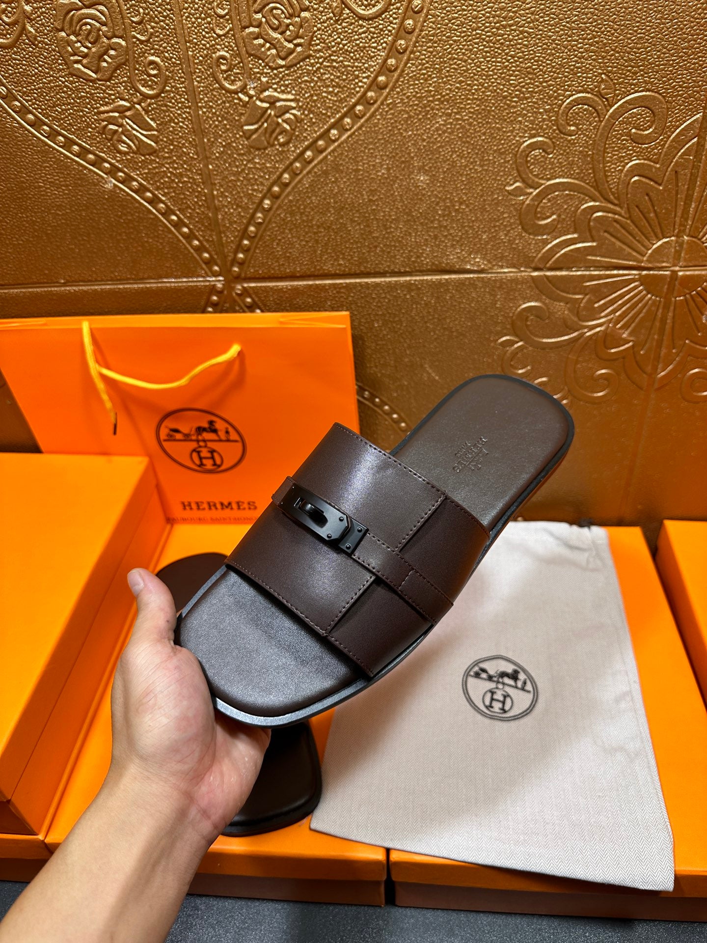 Brown leather slide sandals with buckle strap, angled view held in hand.