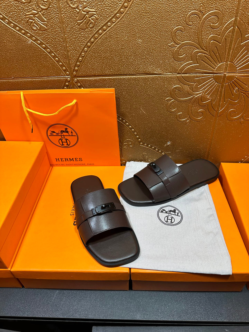 Hermes slide sandals pair with dark buckle straps, placed side-by-side on dust bag.