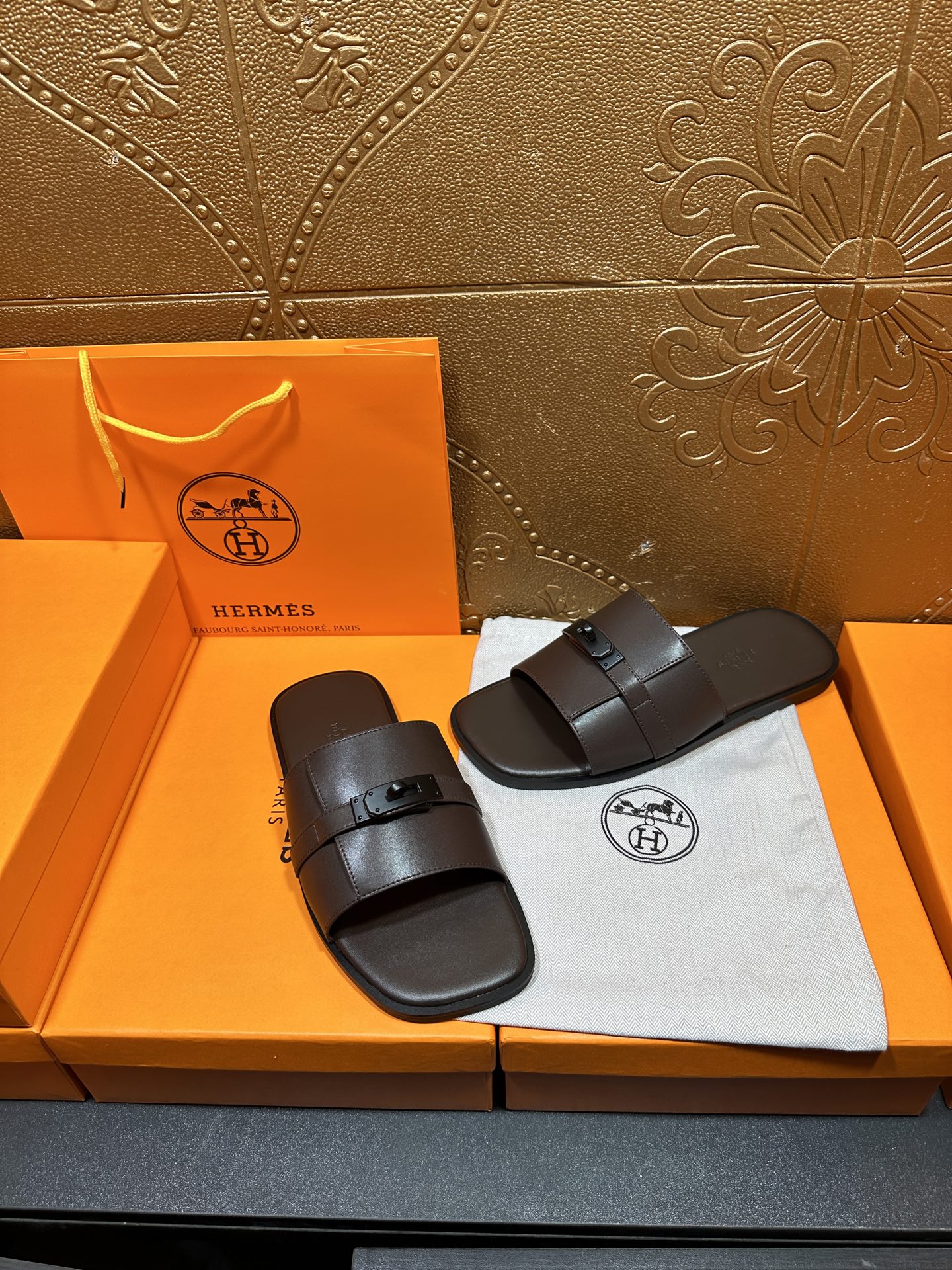 Hermes slide sandals pair with dark buckle straps, placed side-by-side on dust bag.