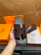 Brown leather slide sandal held up, embossed logo on top strap