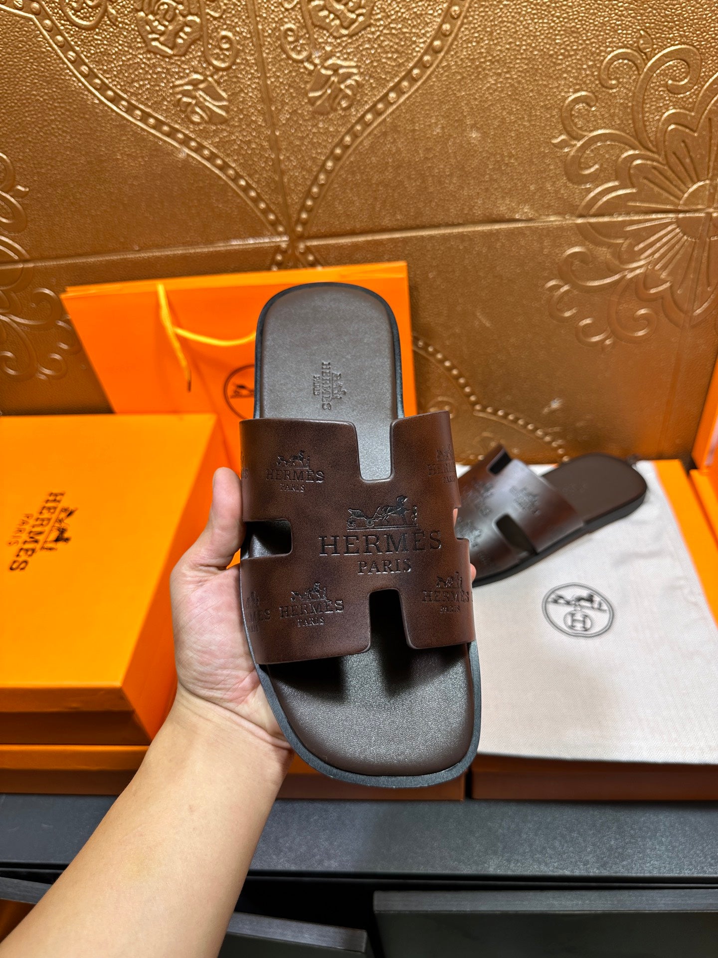 Brown leather slide sandal held up, embossed logo on top strap