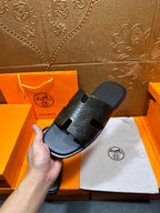 Hermes black slide sandal held in hand with embossed straps and open toe