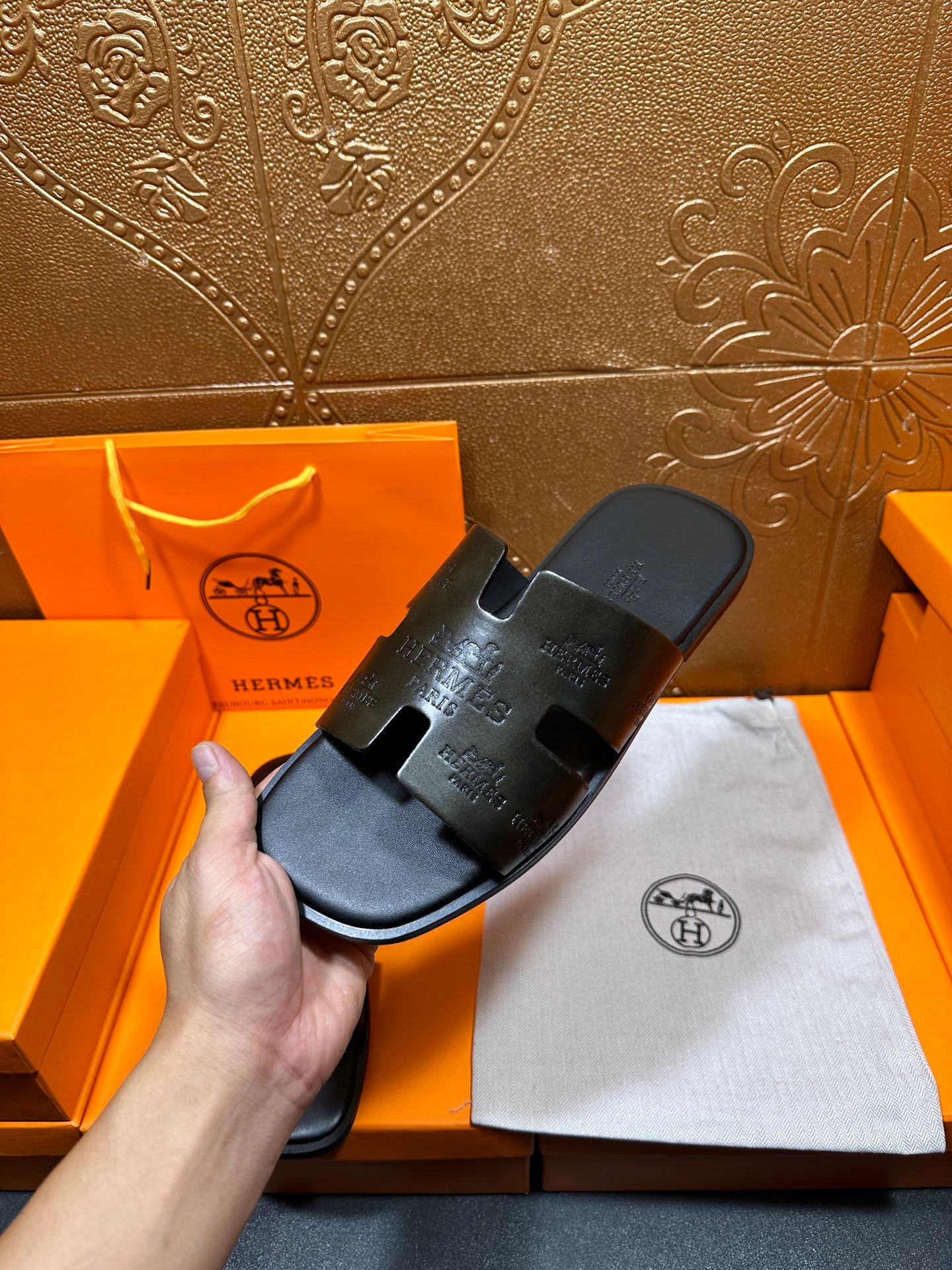 Hermes black slide sandal held in hand with embossed straps and open toe
