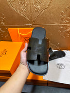 Hermes black slide sandal held in hand, embossed upper and open toe