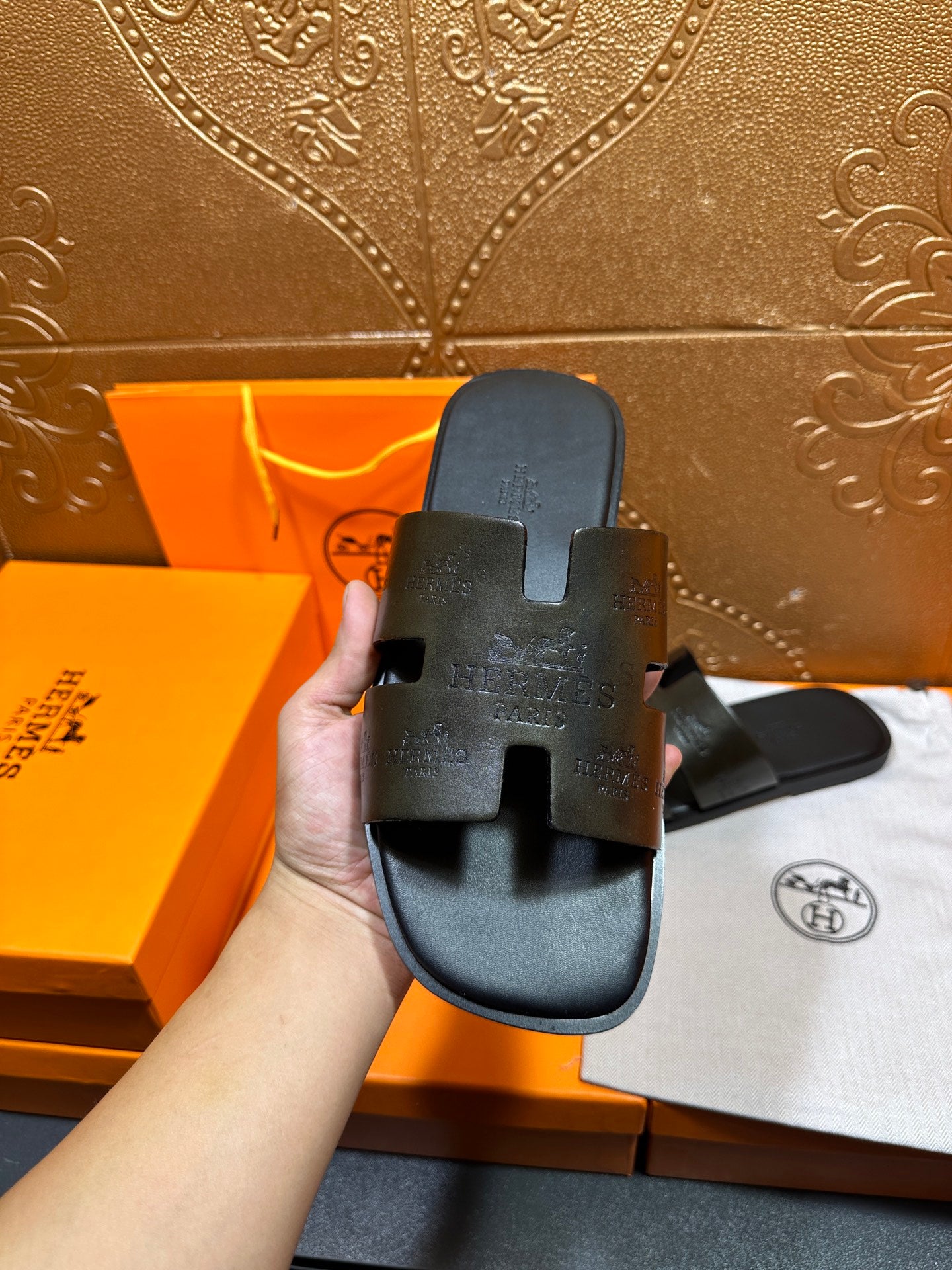Hermes black slide sandal held in hand, embossed upper and open toe