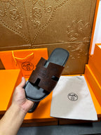 Hermes slide sandals on display; black molded footbed and dark embossed strap