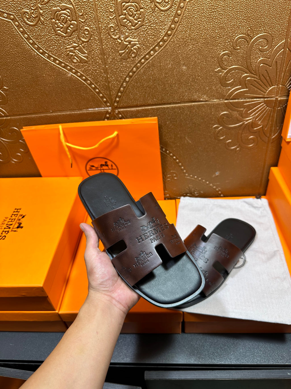 Black Hermes slide sandals held in hand; molded footbed with embossed strap branding