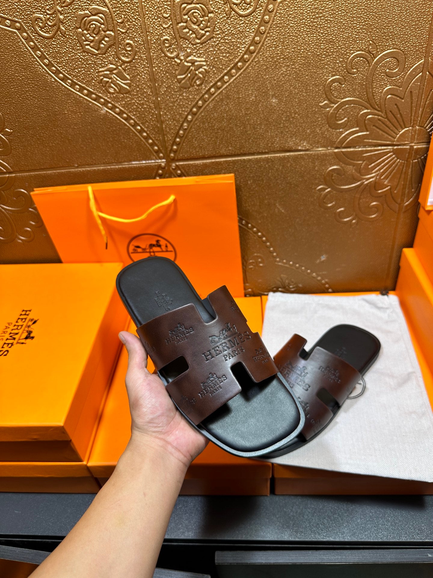 Black Hermes slide sandals held in hand; molded footbed with embossed strap branding