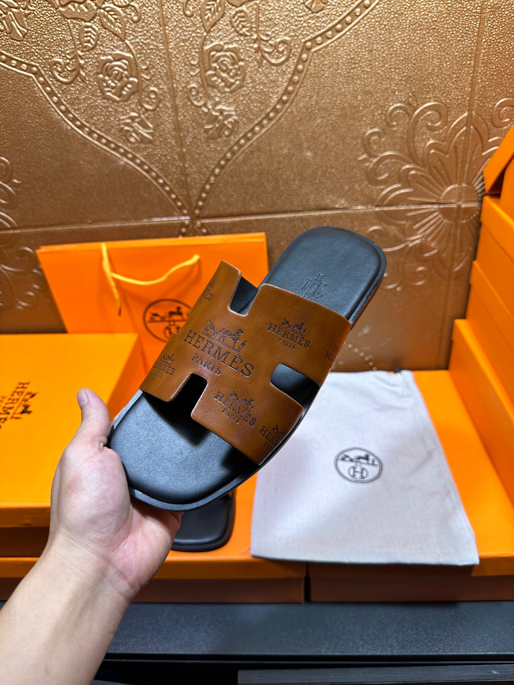 Hermes slide sandals with tan embossed straps and dark soles, displayed on cloth.