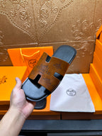 Hermes slide sandals with tan embossed straps and dark soles, displayed on cloth.