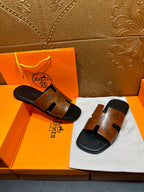 Hermes slide sandals with tan embossed straps and dark soles on presentation cloth.