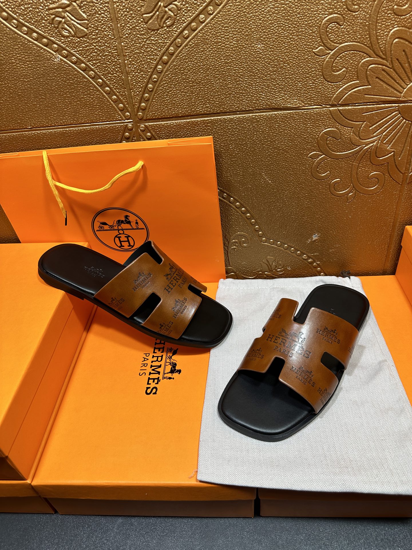 Hermes slide sandals with tan embossed straps and dark soles on presentation cloth.