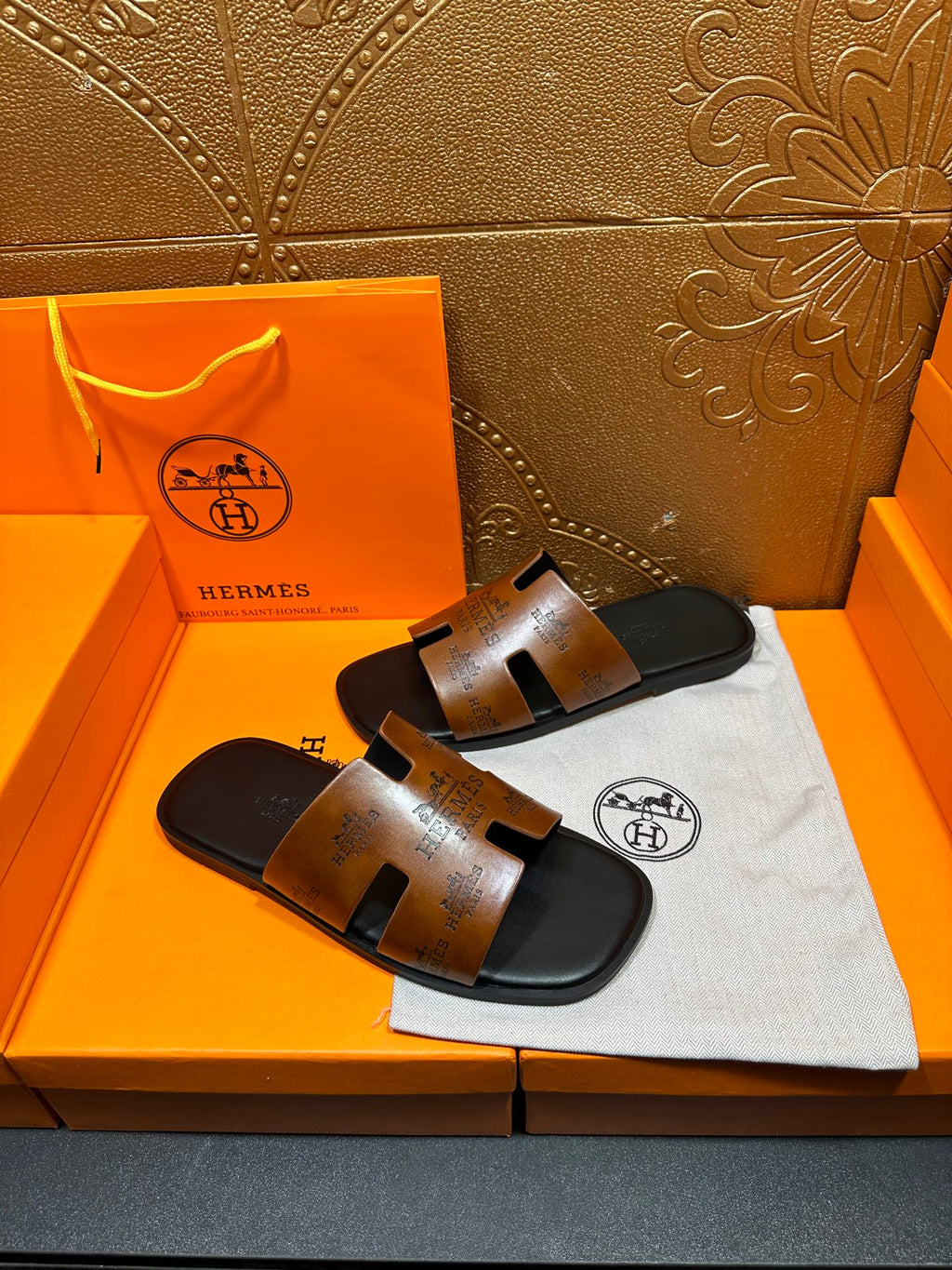 Hermes slide sandals on dust bag, tan embossed straps and dark rubber soles.