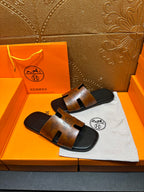 Hermes slide sandals on dust bag, tan embossed straps and dark rubber soles.