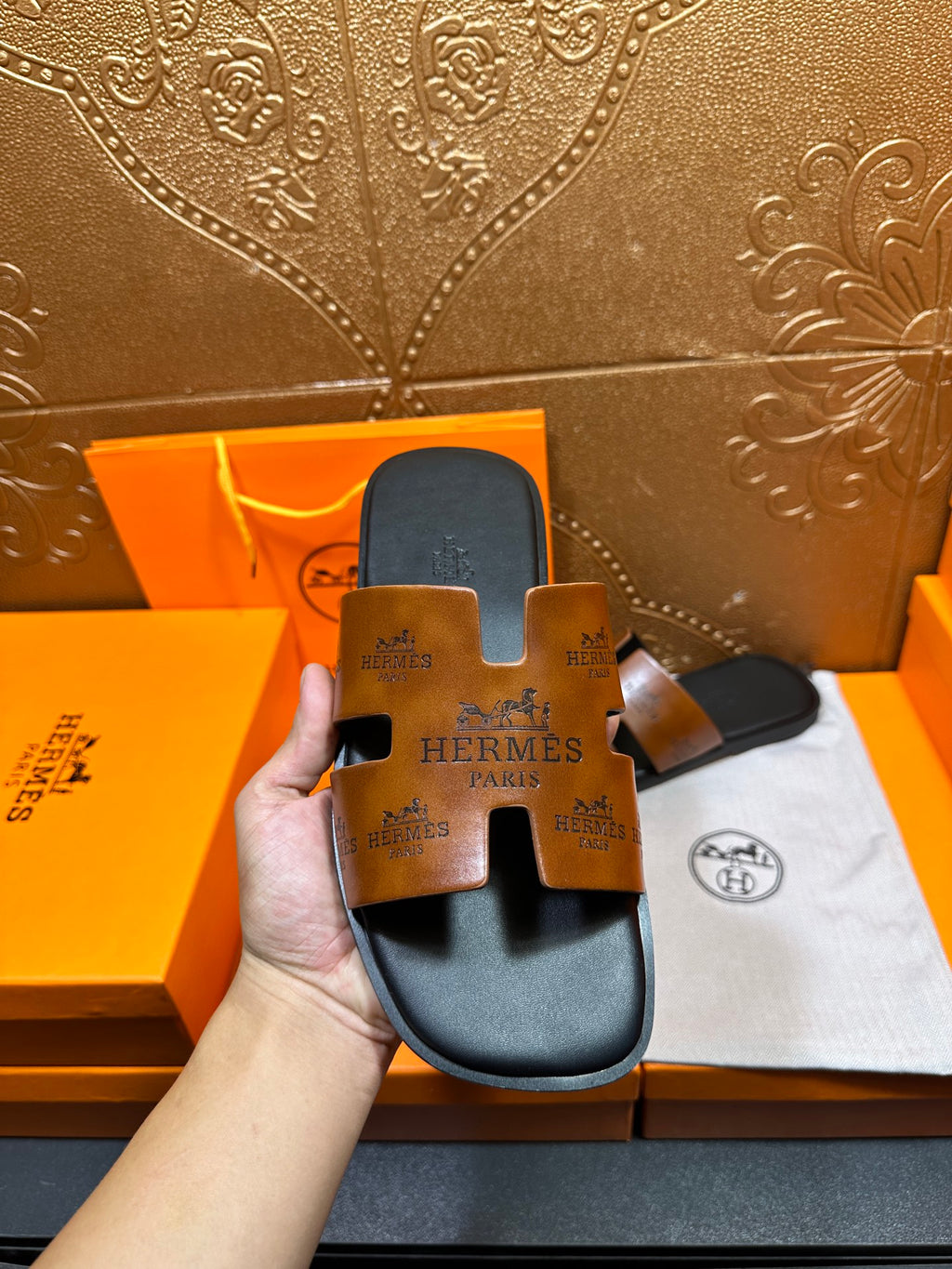 Hermes slide sandal close-up showing tan embossed logo straps and dark footbed.