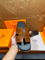 Hermes slide sandal close-up showing tan embossed logo straps and dark footbed.