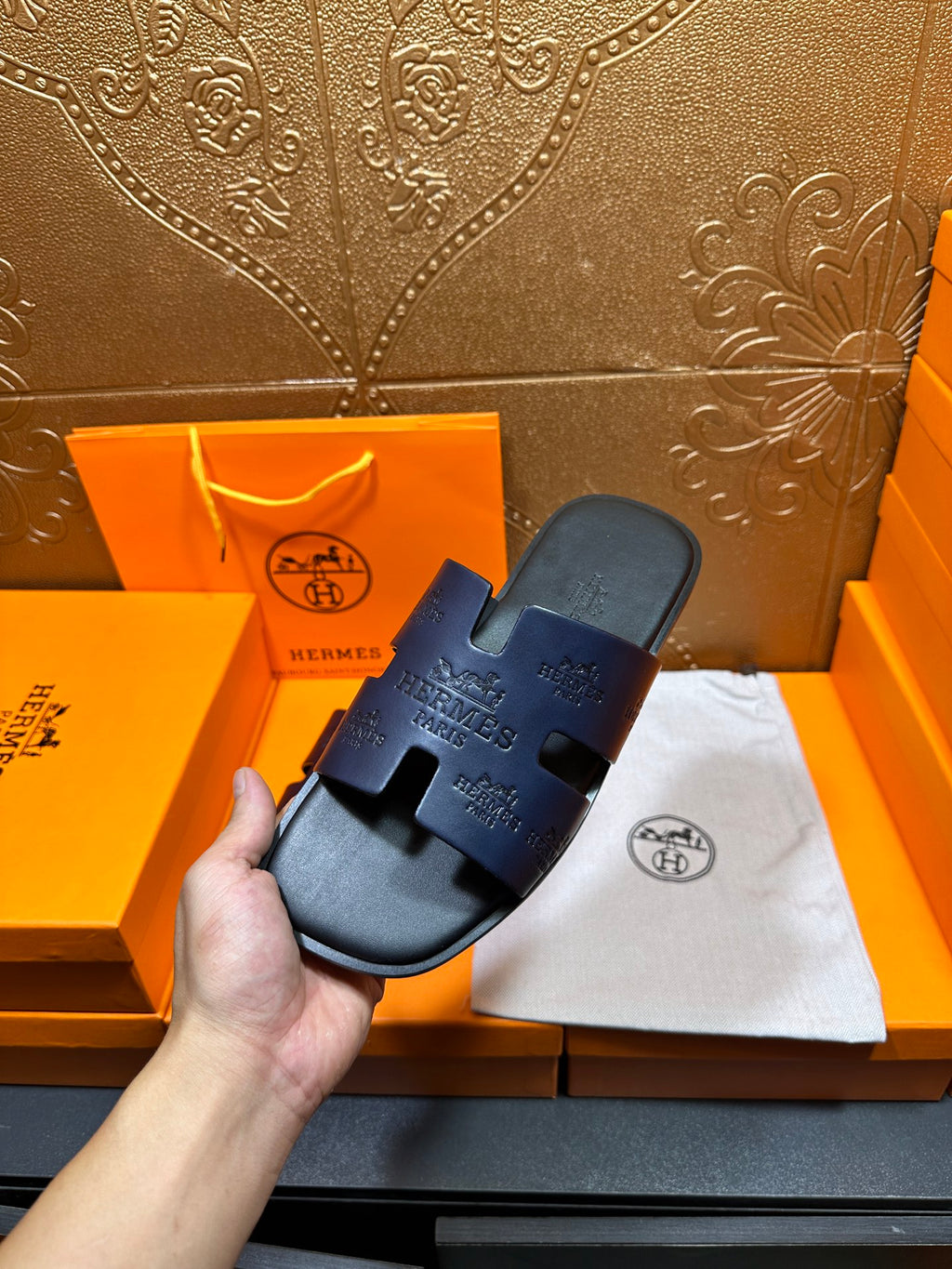Hermes slide sandals in dark blue held in hand, single sandal on white cloth
