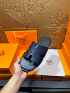 Hermes slide sandals in dark blue held in hand, single sandal on white cloth