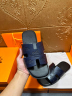 Hermes slide sandals in dark blue held up, front straps with embossed logo
