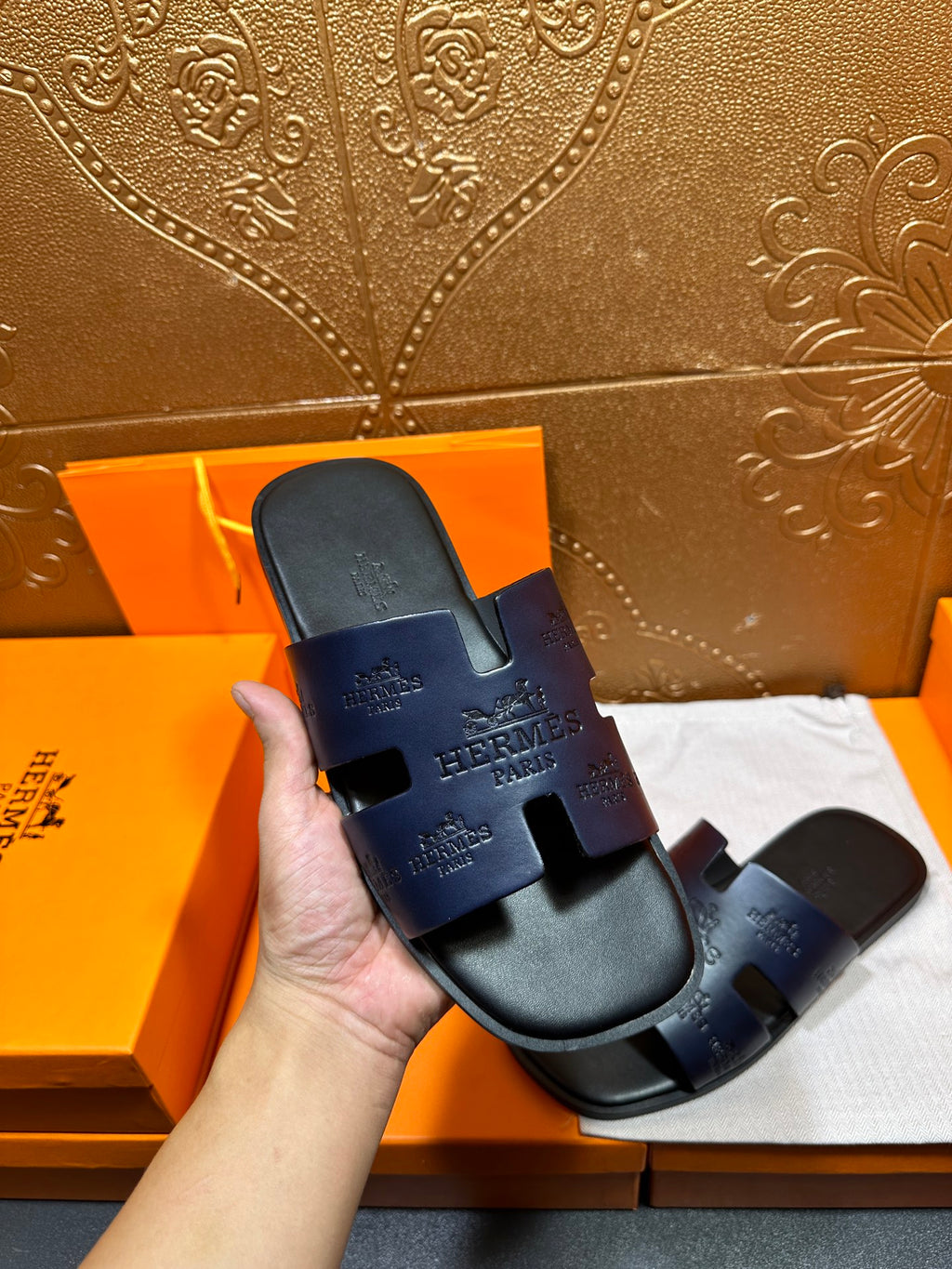 Hermes slide sandals in dark blue held in hand, showing embossed logos on straps