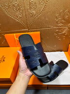 Hermes slide sandals in dark blue held in hand, showing embossed logos on straps