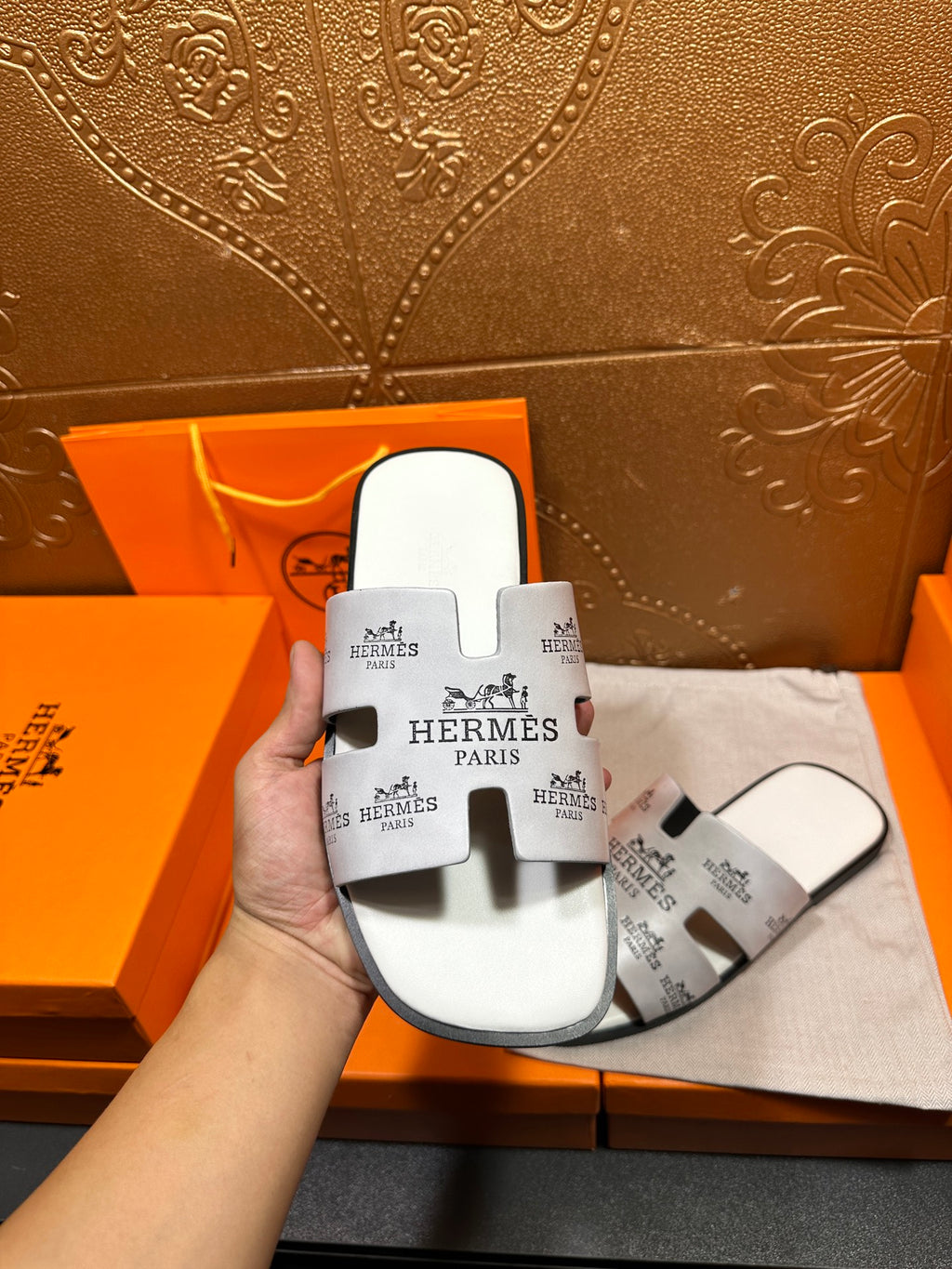 Hermes white slide sandals held in hand, open toe and black logo straps