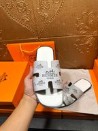 Hermes white slide sandals held in hand, open toe and black logo straps