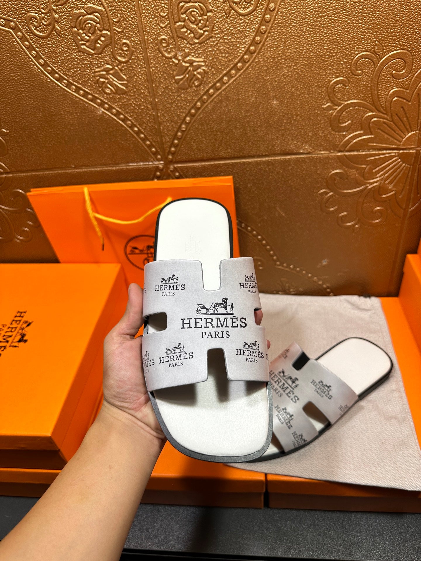 Hermes white slide sandals held in hand, open toe and black logo straps