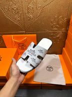 Hermes white slide sandal held in hand, black logo print straps