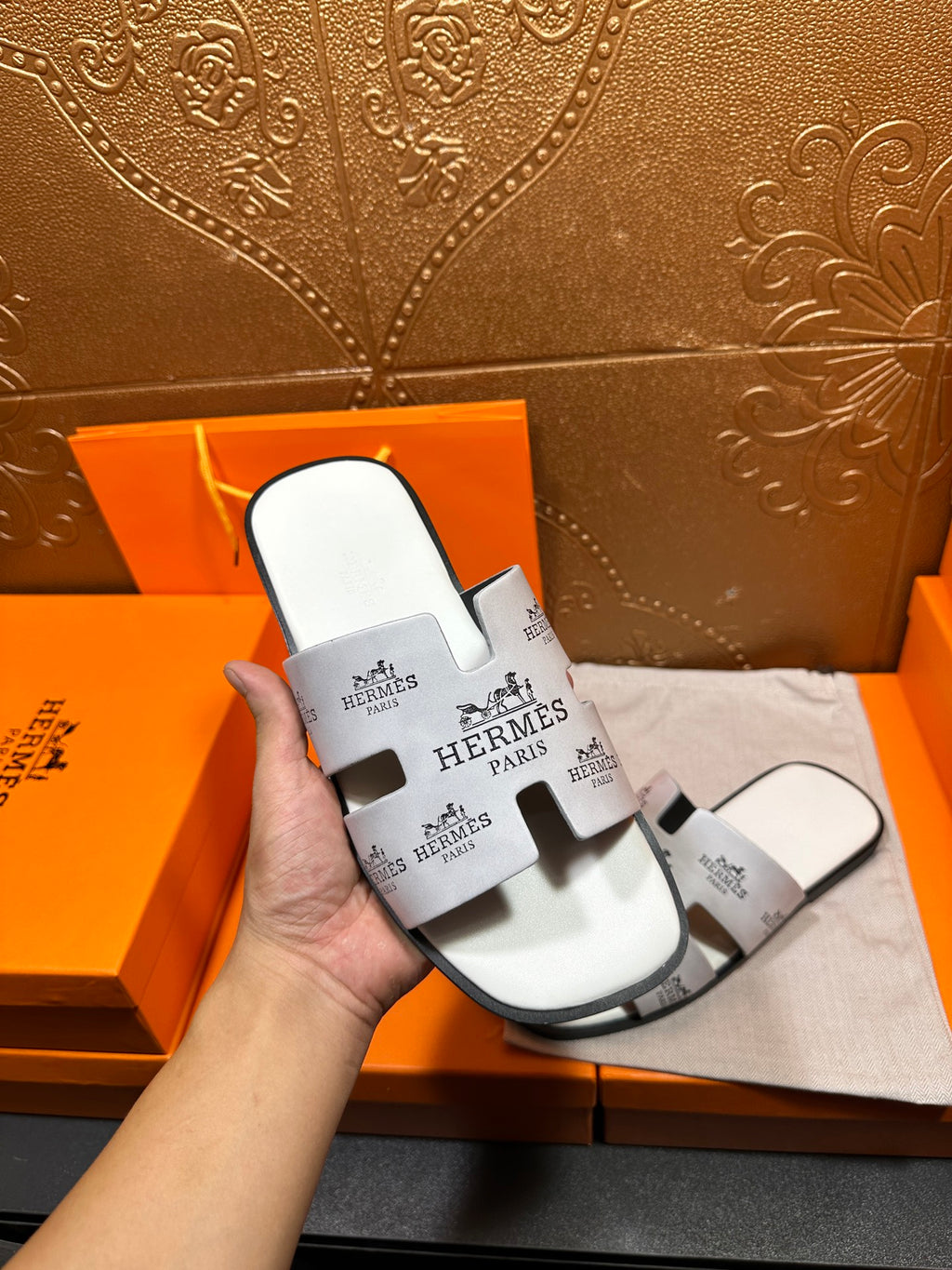 Hermes white slide sandal held in hand, black logo print straps