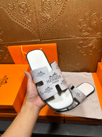 Hermes white slide sandal held in hand, black logo print straps