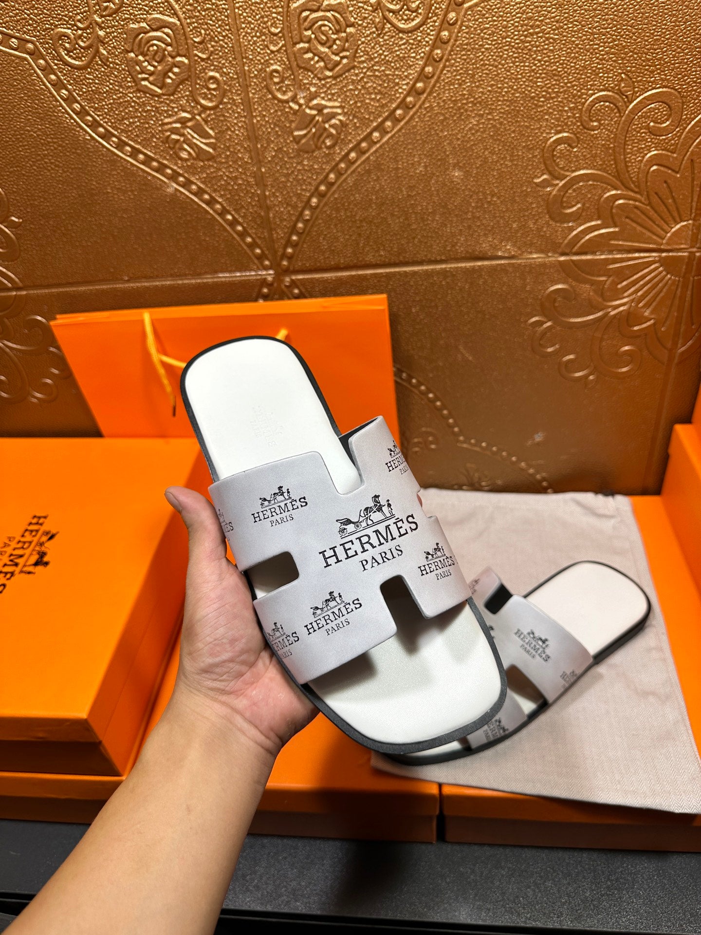 Hermes white slide sandal held in hand, black logo print straps
