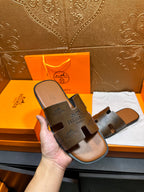 Hand holding dark gray logo slide sandal with thick strap and flat sole