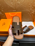 Hand holding dark gray slide sandal with embossed brand on footbed
