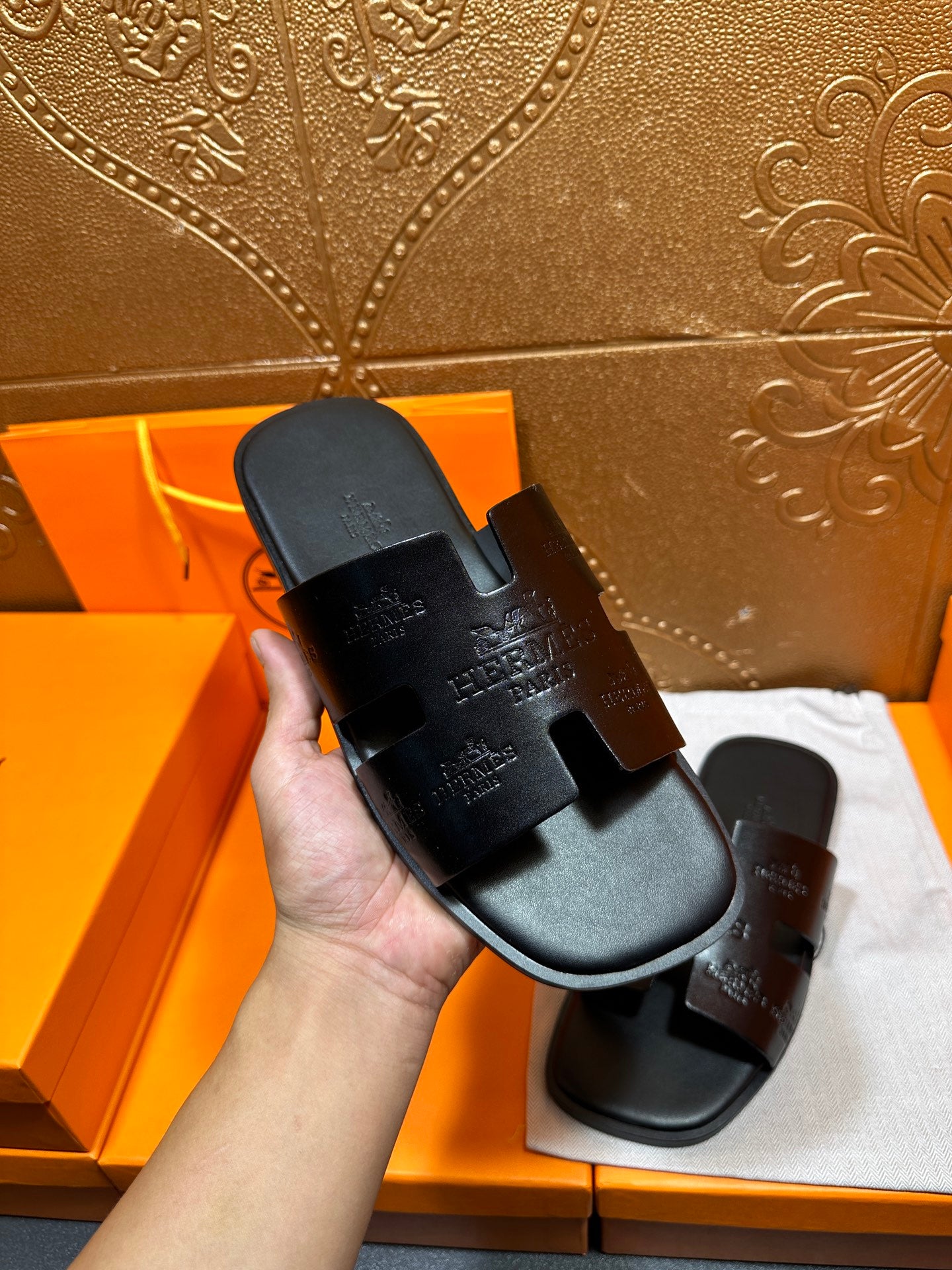 Hermes black slide sandal held in hand, embossed cross-strap design