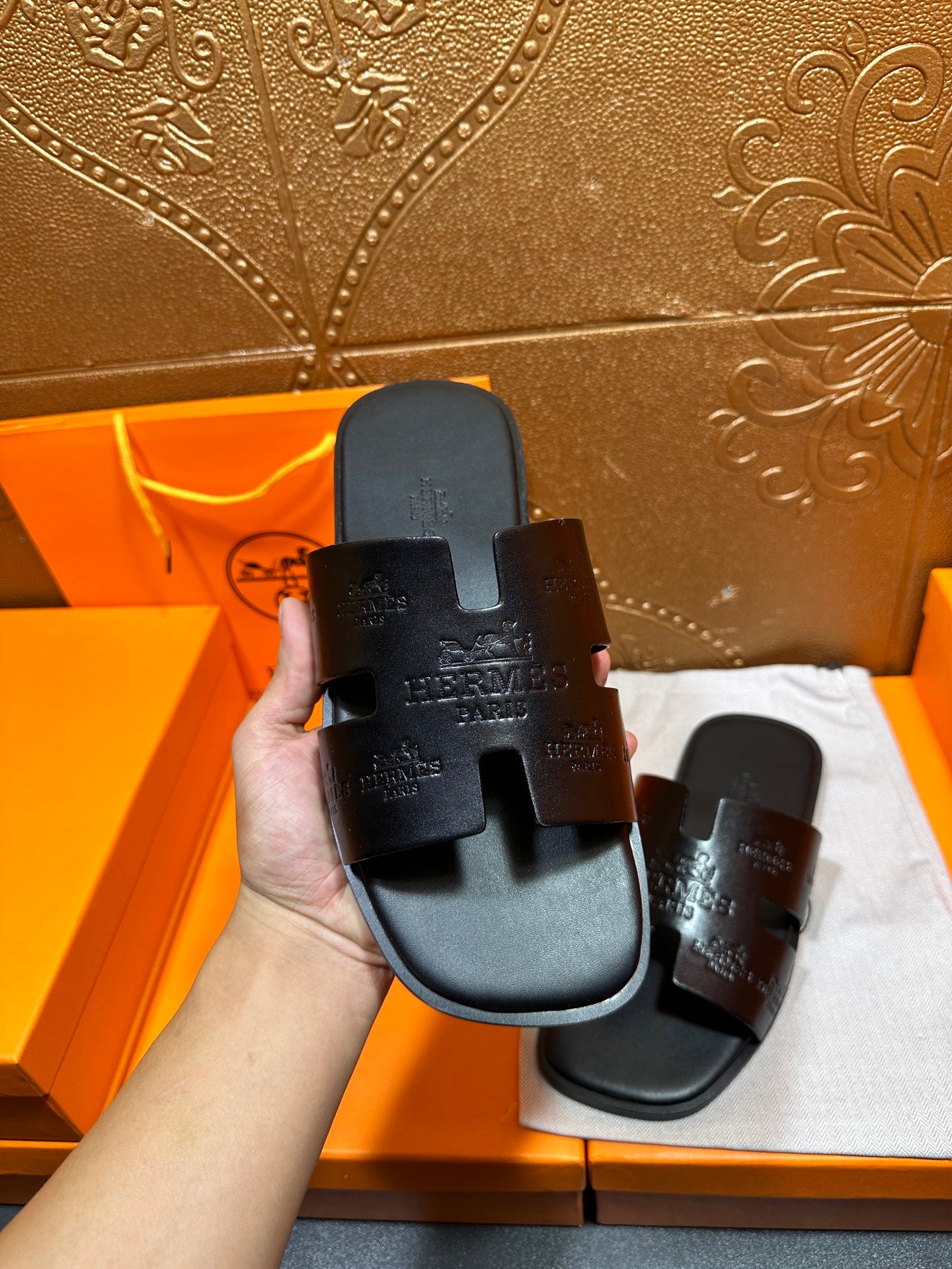 Hermes black slide sandal held in hand, embossed strap and molded footbed