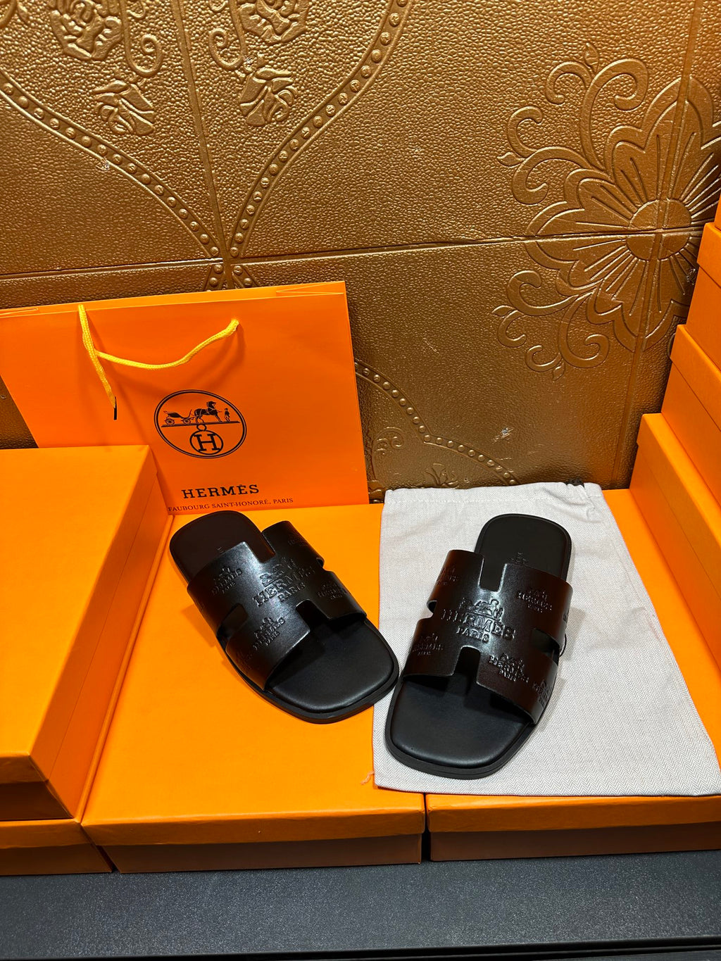 Hermes black slide sandals on white cloth, embossed strap detail visible