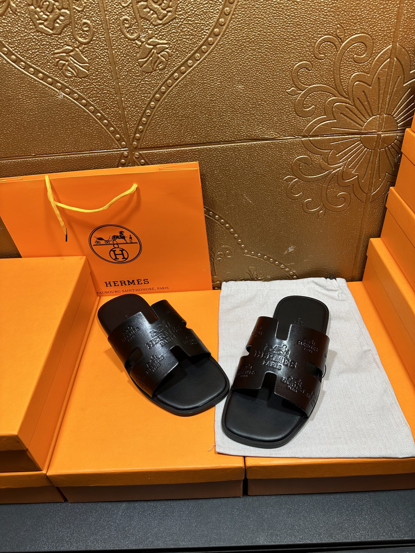 Hermes black slide sandals on white cloth, embossed strap detail visible