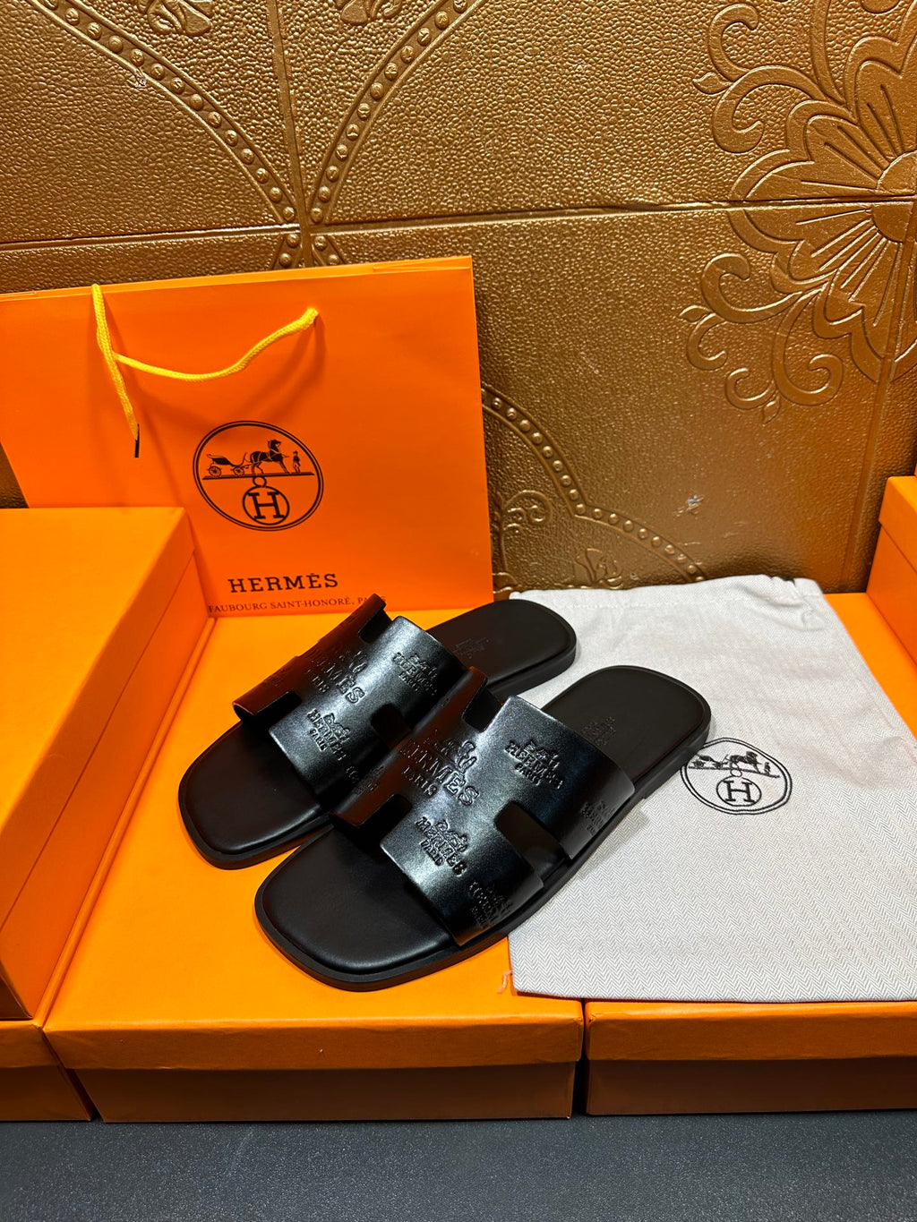 Hermes black slide sandals with embossed logo straps, arranged on white cloth