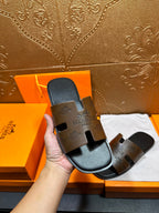 Hermes slide sandals held in hand, dark brown logo straps with black footbed