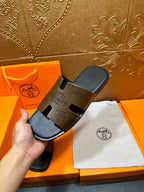 Hermes slide sandals held in hand, dark brown embossed strap design