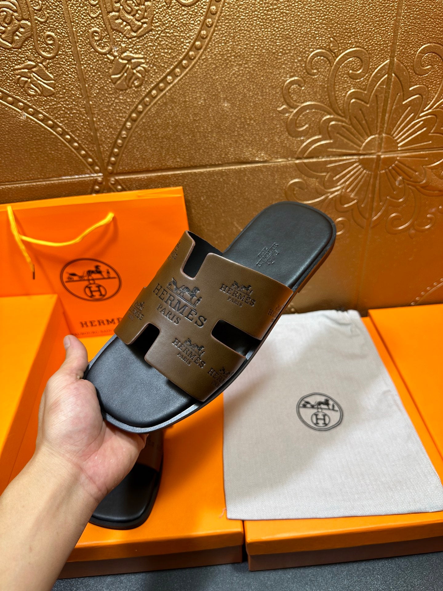 Hermes slide sandals held in hand, dark brown embossed strap design