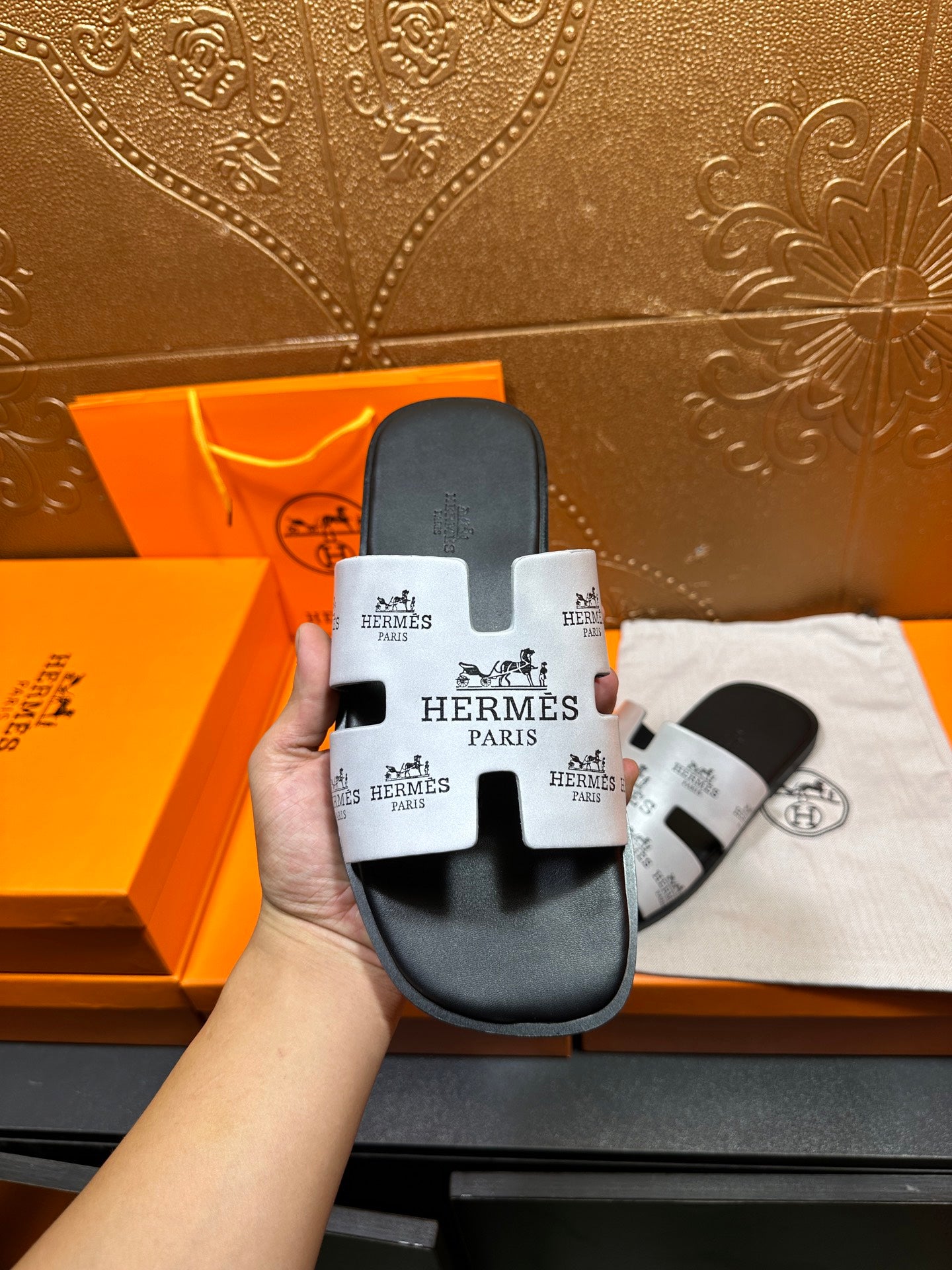 Hand holding Hermes slide sandal, dark gray with white logo strap