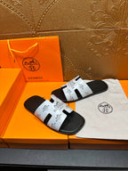 Hermes slide sandals with white logo strap and black sole, side-by-side