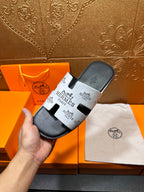 Hermes slide sandal held in hand, dark gray with white logo strap