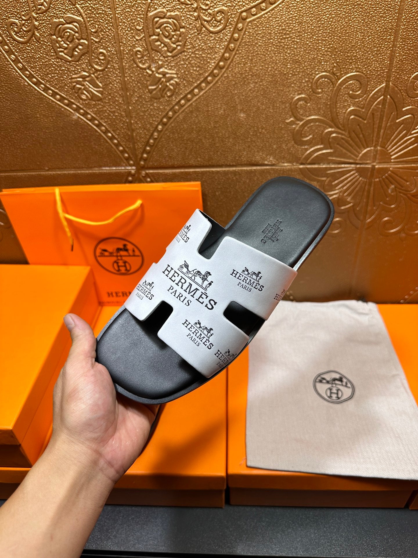 Hermes slide sandal held in hand, dark gray with white logo strap